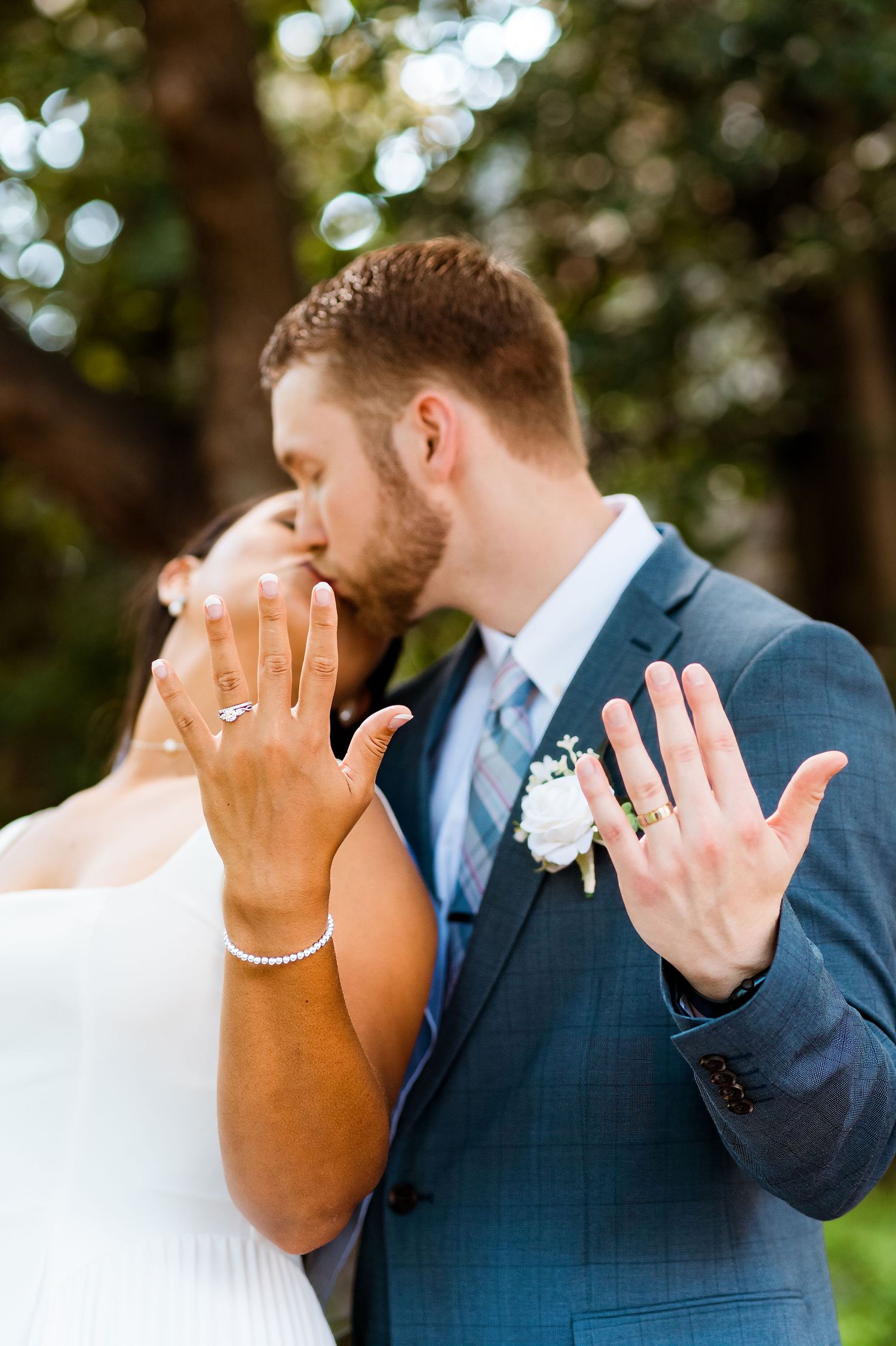 Newlyweds showing off their wedding rings in an intimate moment in a garden setting with bokeh lighting.