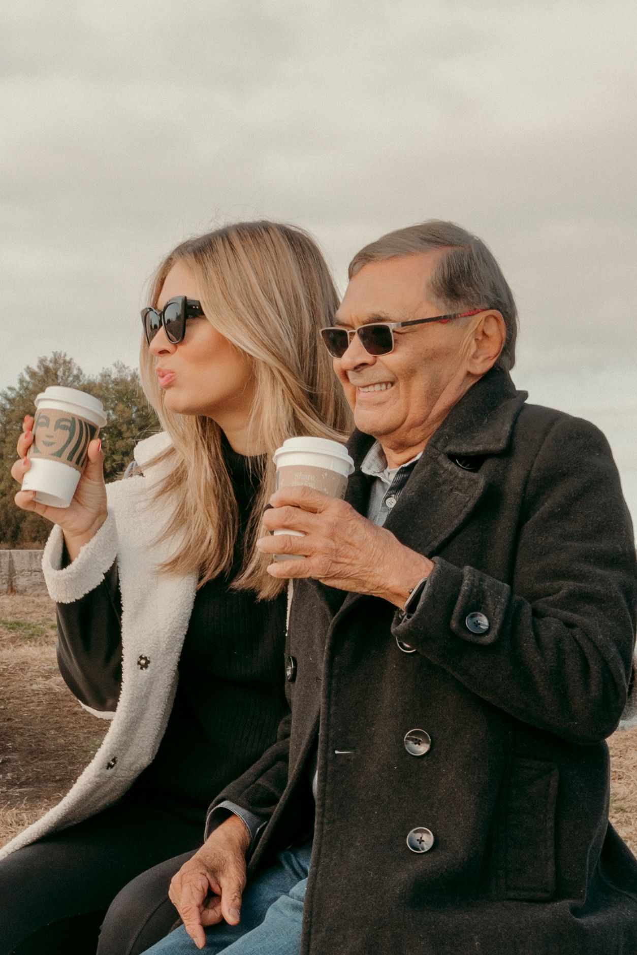 Two people in stylish winter coats sharing coffee and conversation outdoors.
