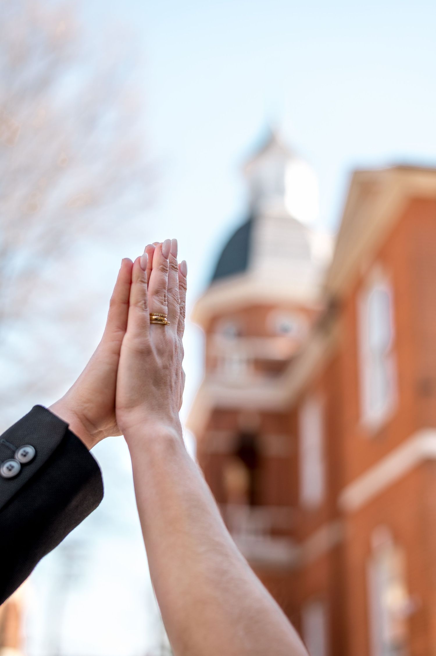 Close-up of hands showing wedding rings with brick building in background.