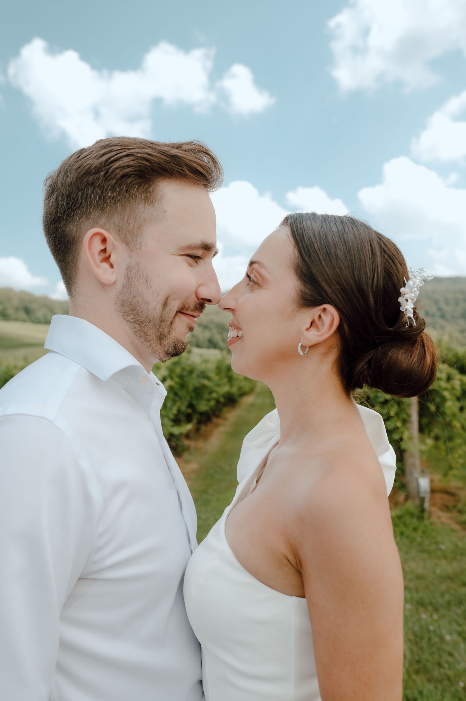 A couple shares intimate moments outdoors in a series of candid photos with green hills and cloudy skies in the background.