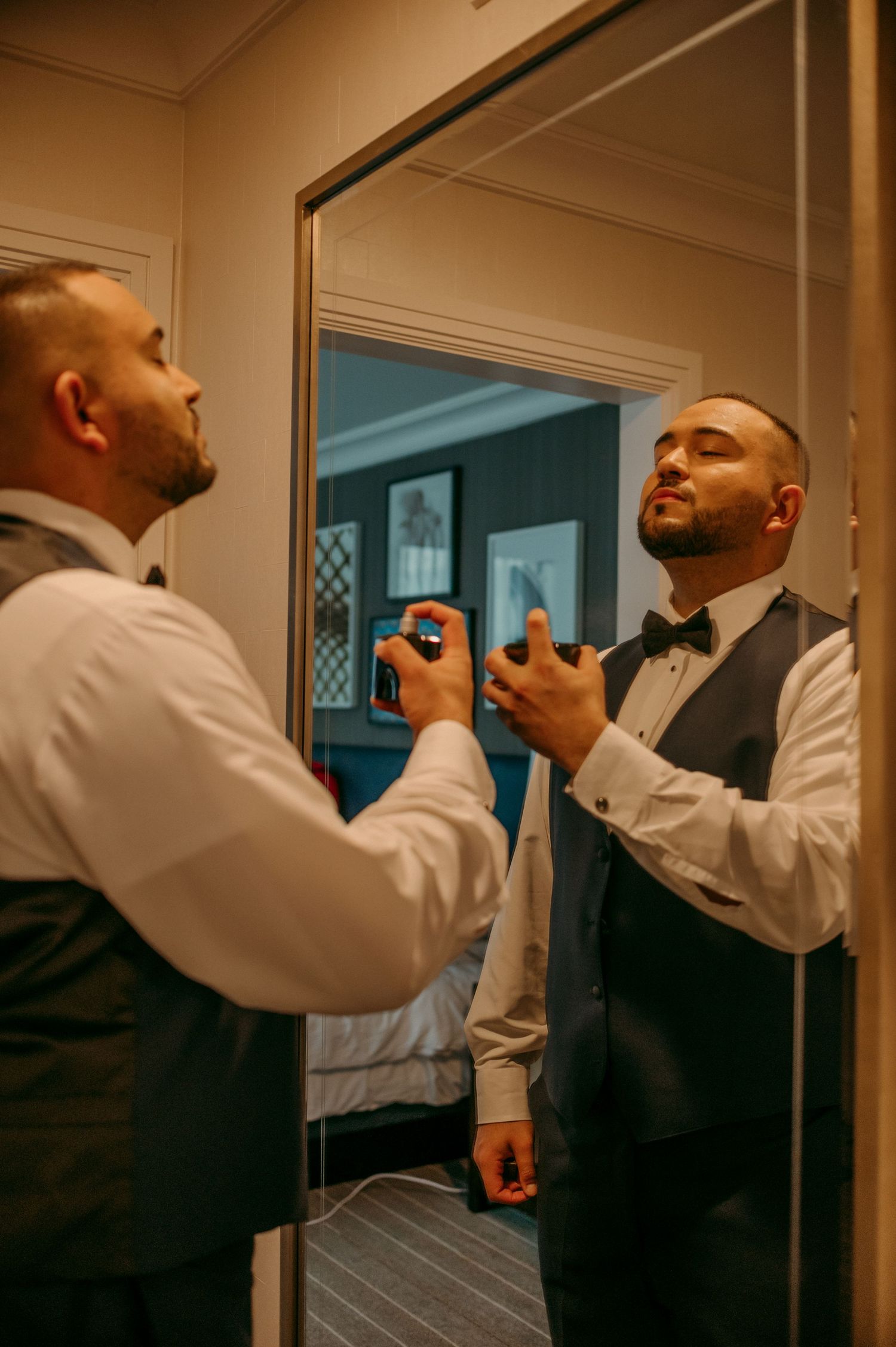 Reflection in mirror shows person in formal attire adjusting bow tie while getting ready.