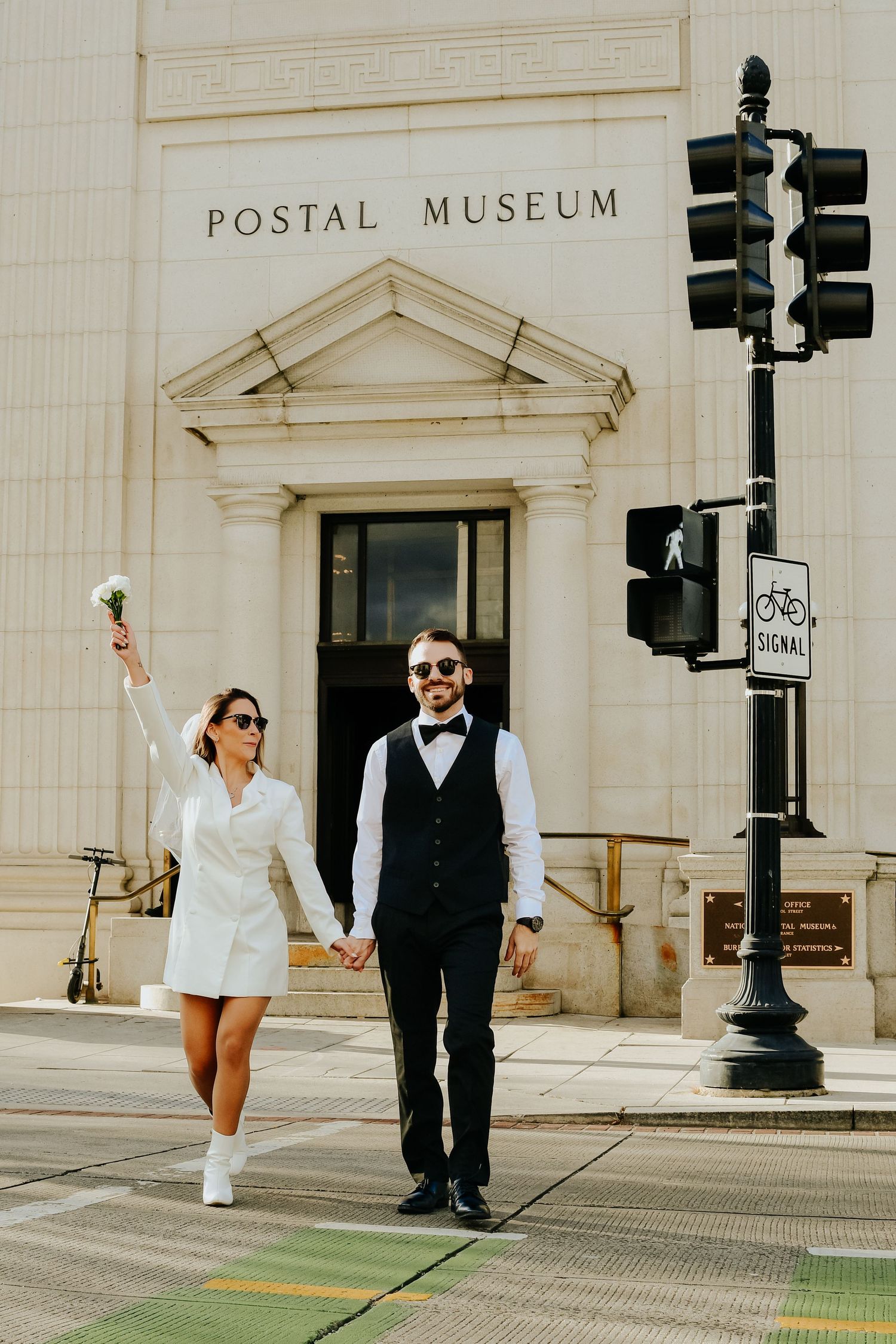 A couple poses in front of the Postal Museum building entrance near a vintage street light and traffic signal.