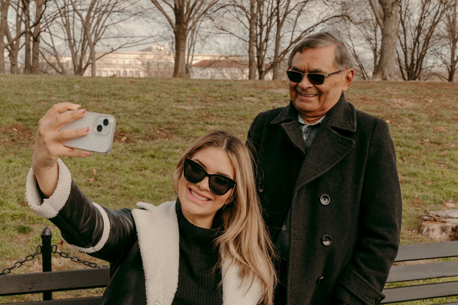 Two people taking a selfie together while sitting on a park bench on a sunny day.