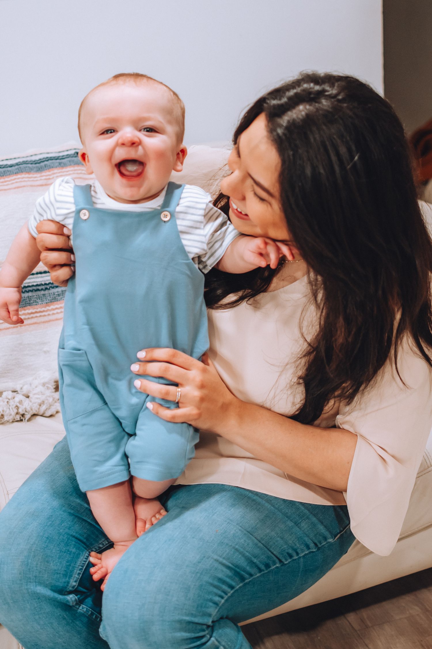 A joyful baby in blue overalls sharing a laugh with mother.