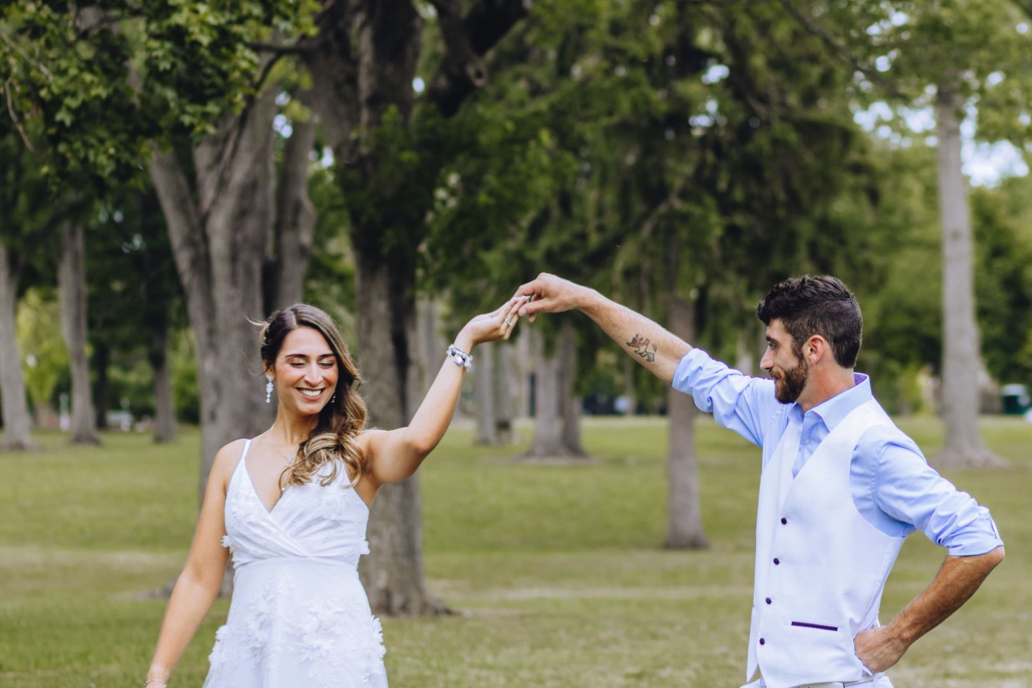 A couple dancing and twirling together in a sunny park with green trees in the background.