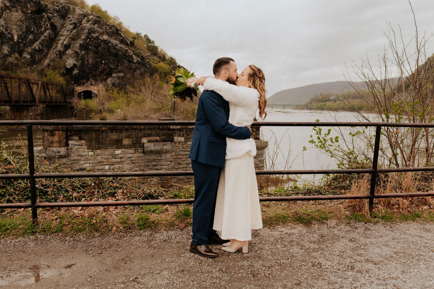 A couple embrace on a viewpoint overlooking a misty lake with mountains and rugged terrain in the background.