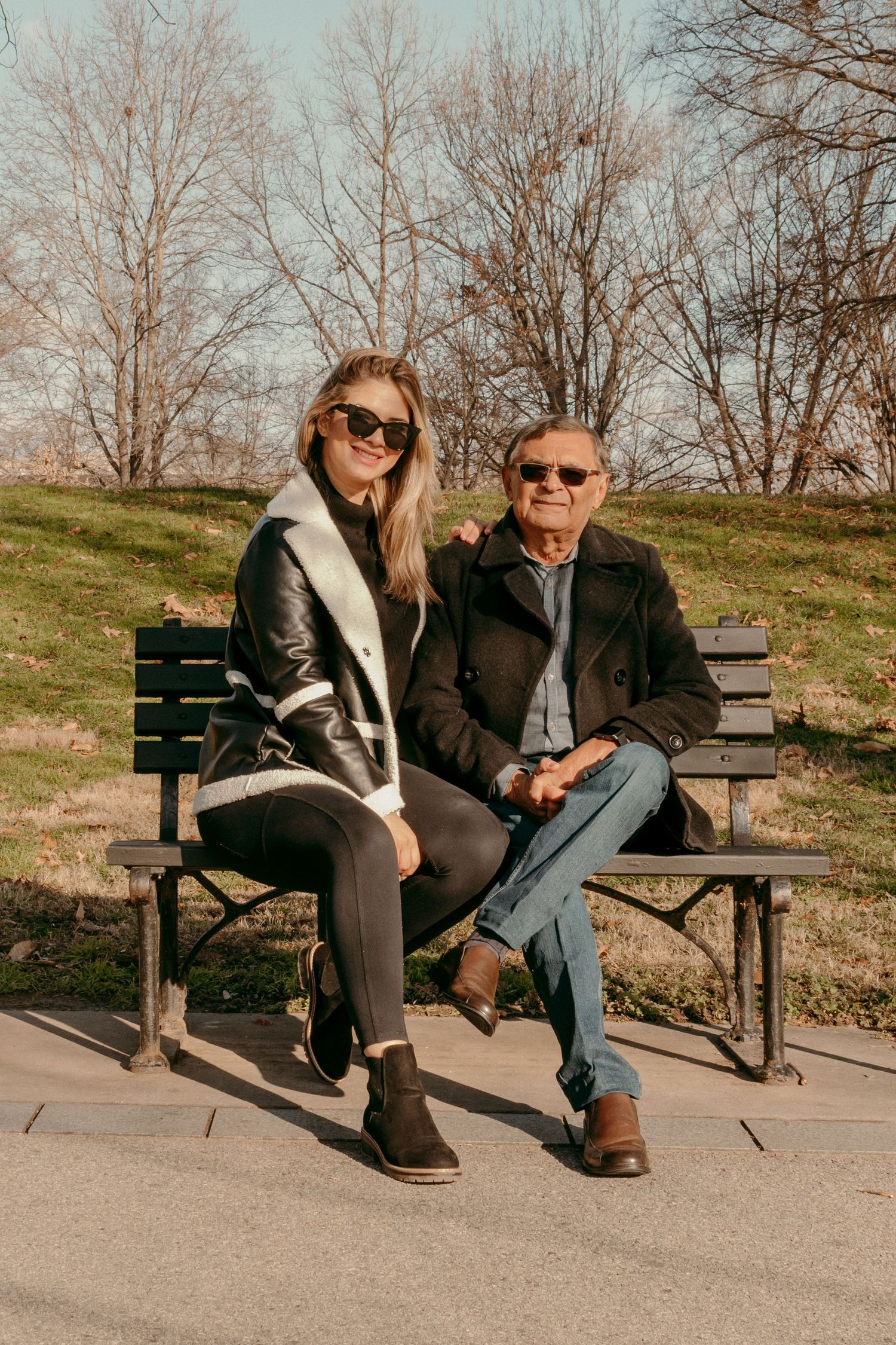 Two people sitting together on park bench wearing coats on autumn day.
