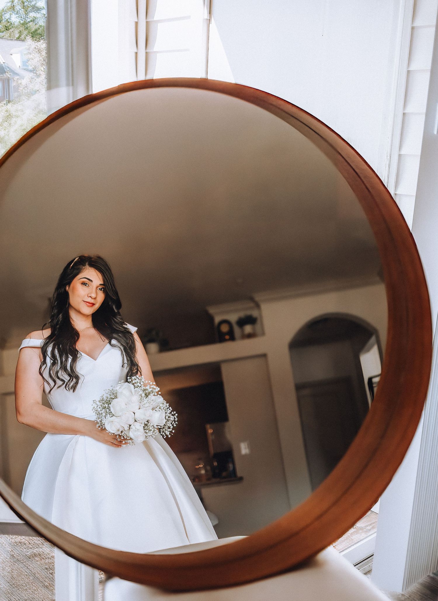 A reflection in a round copper-framed mirror shows a bride in a classic white ballgown holding a bouquet.