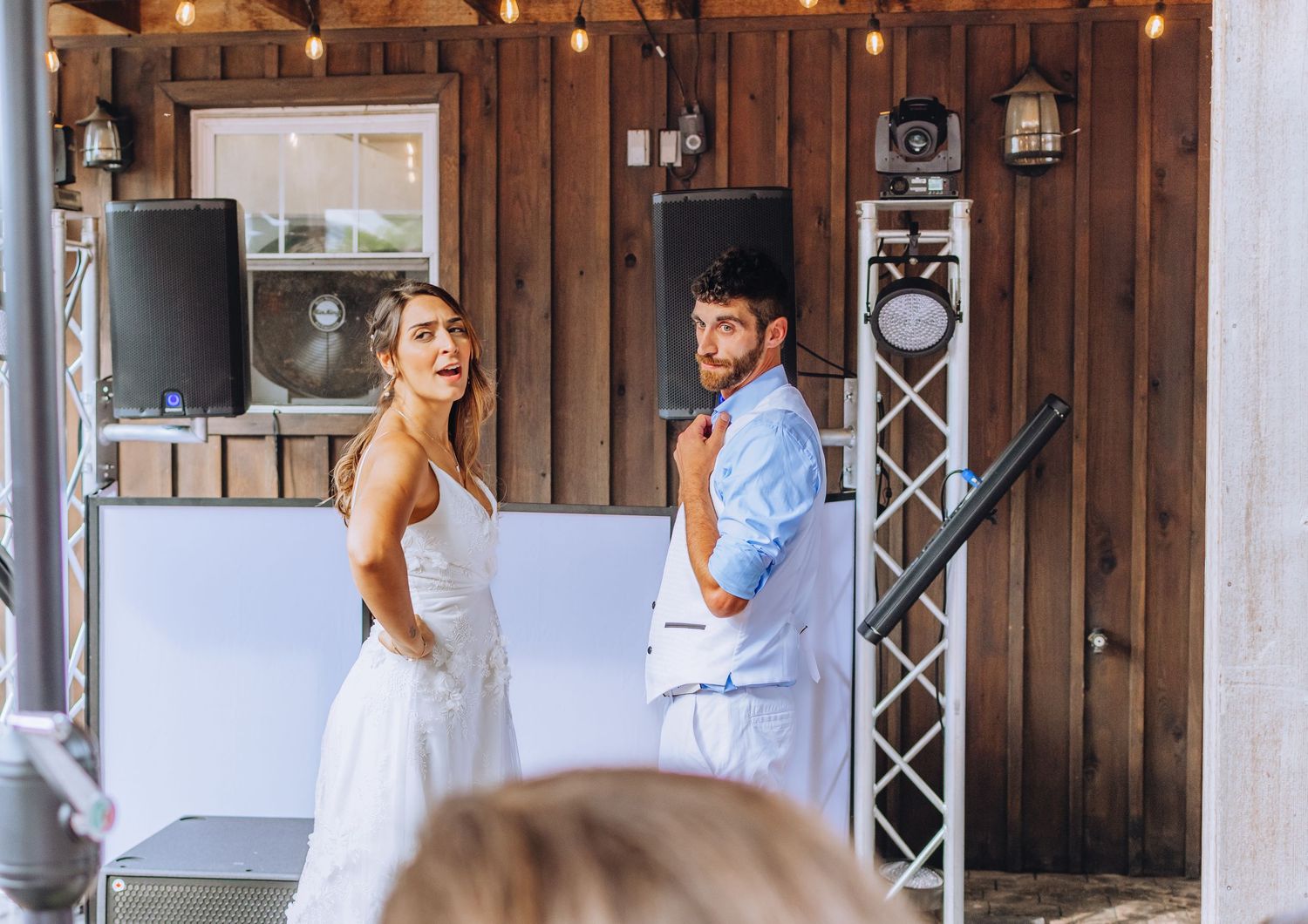 A rustic outdoor wedding ceremony with wooden barn setting and guests seated on benches at sunset.