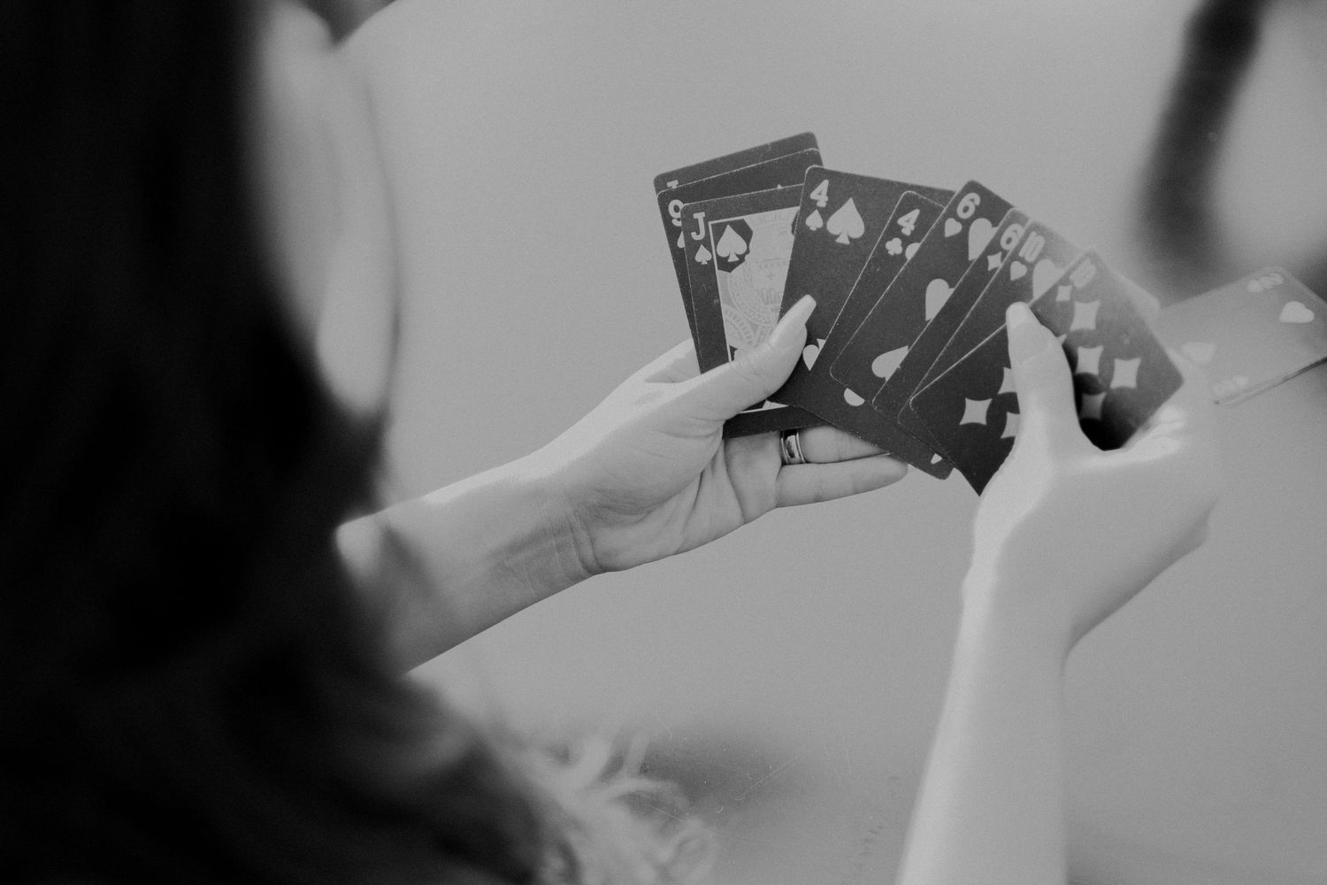 Hands holding playing cards in a black and white photo showing a poker game in progress.