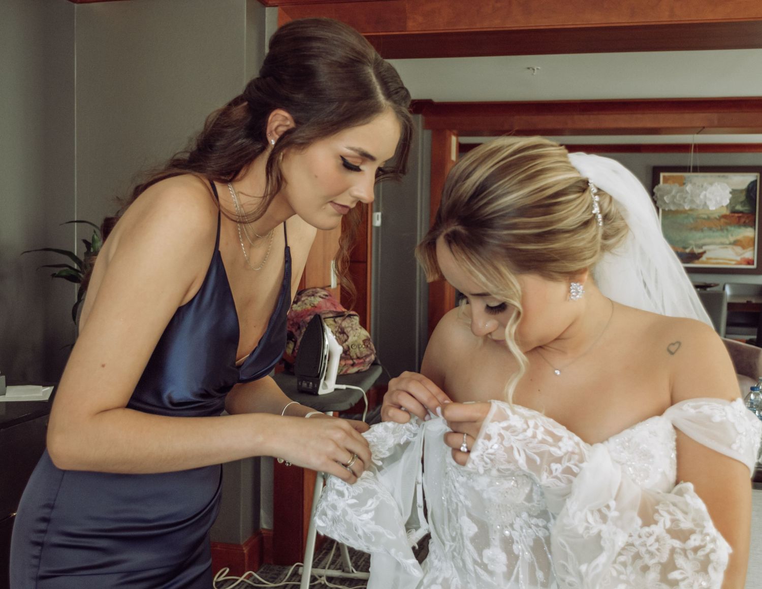 Final adjustments are made to a bride's wedding dress by her attendant during pre-ceremony preparations.