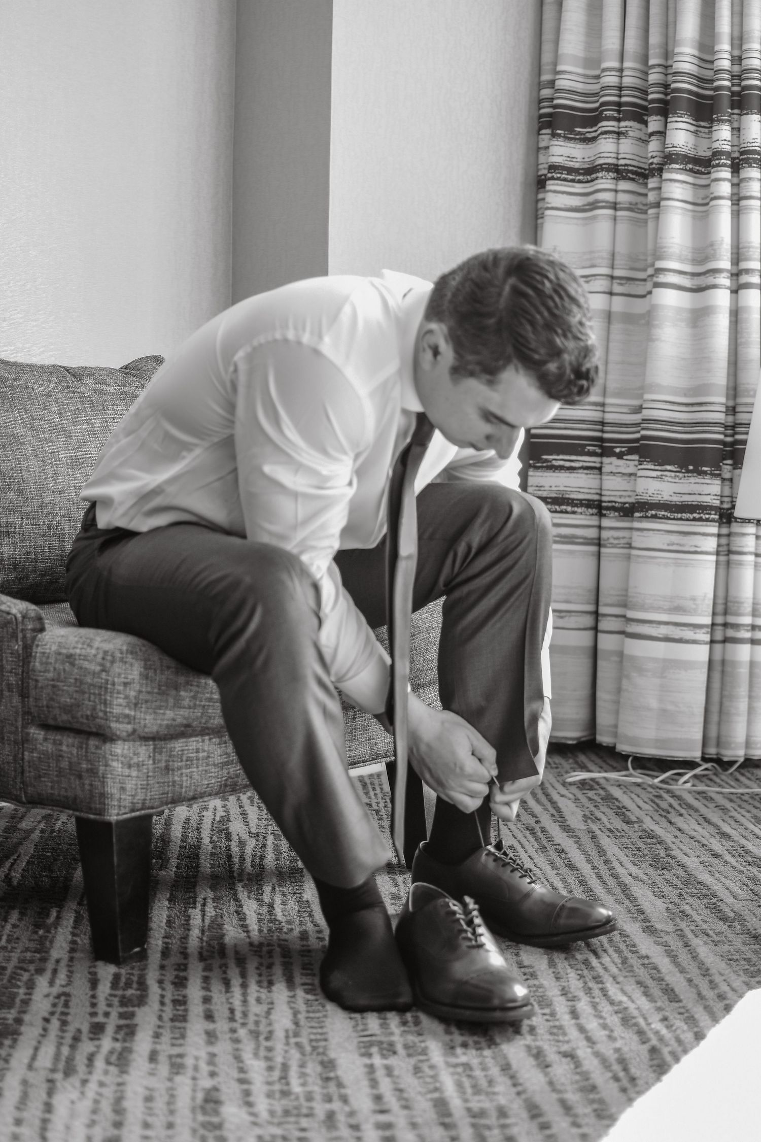 A sequence of black and white photos showing someone tying their dress shoes while sitting on a striped couch.
