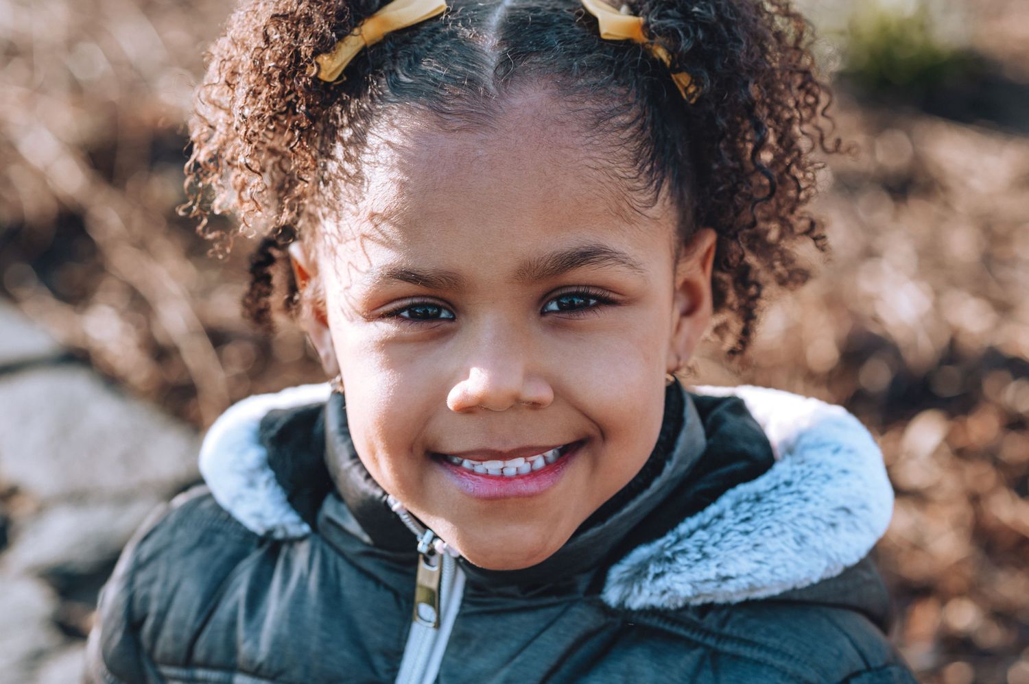 Child in winter coat smiles brightly outdoors.