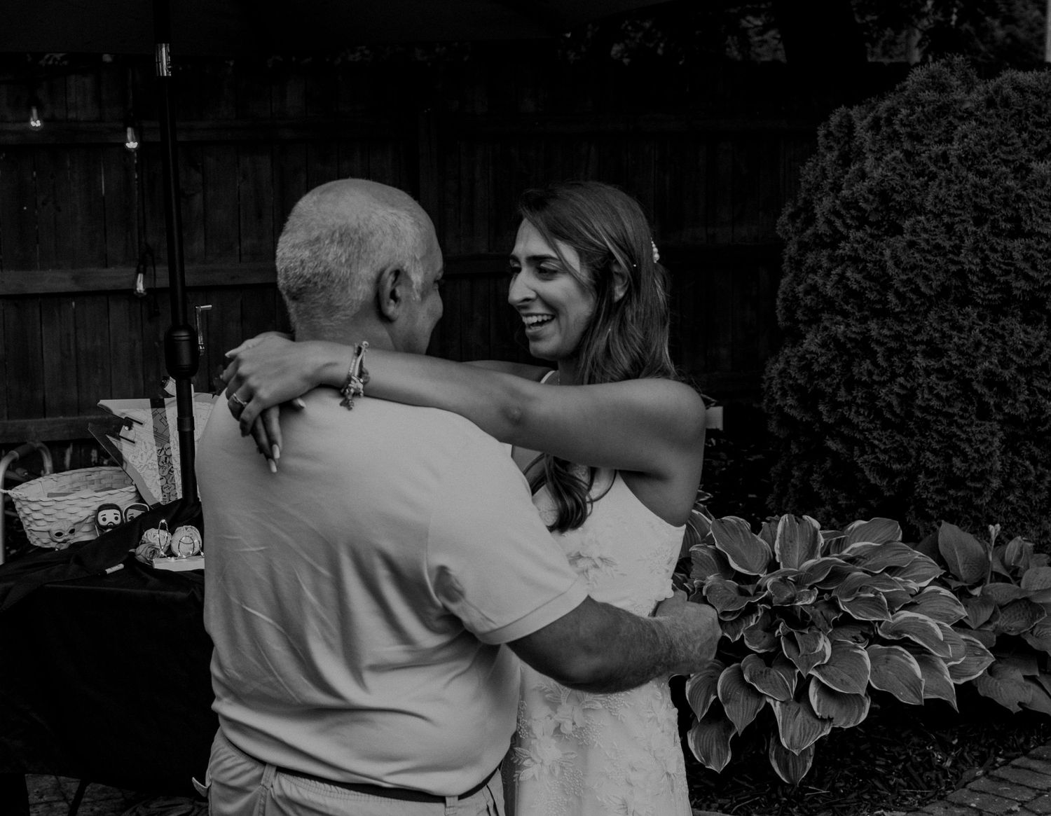 A tender black and white moment of an older person and younger person embracing in a garden with hostas nearby.