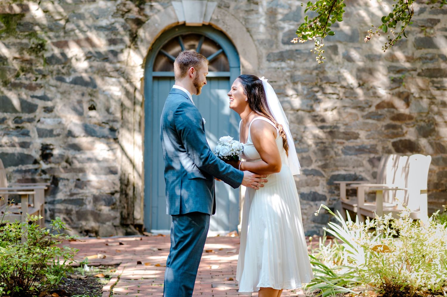 A couple shares an intimate moment in front of a rustic stone wall during their first look wedding photo session.