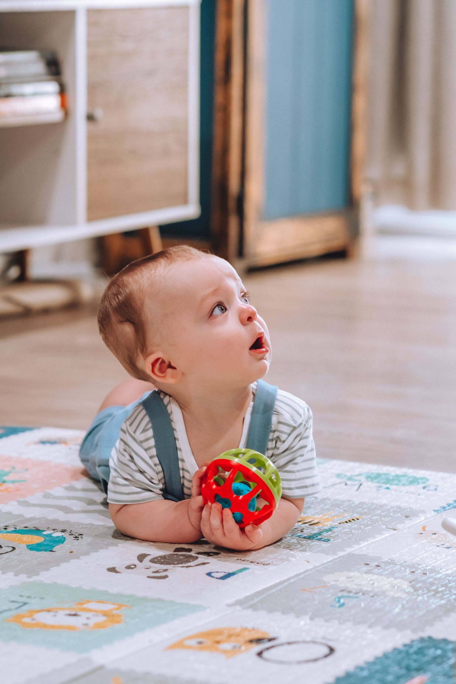 Baby in striped outfit lying on playmat with colorful ball toy.