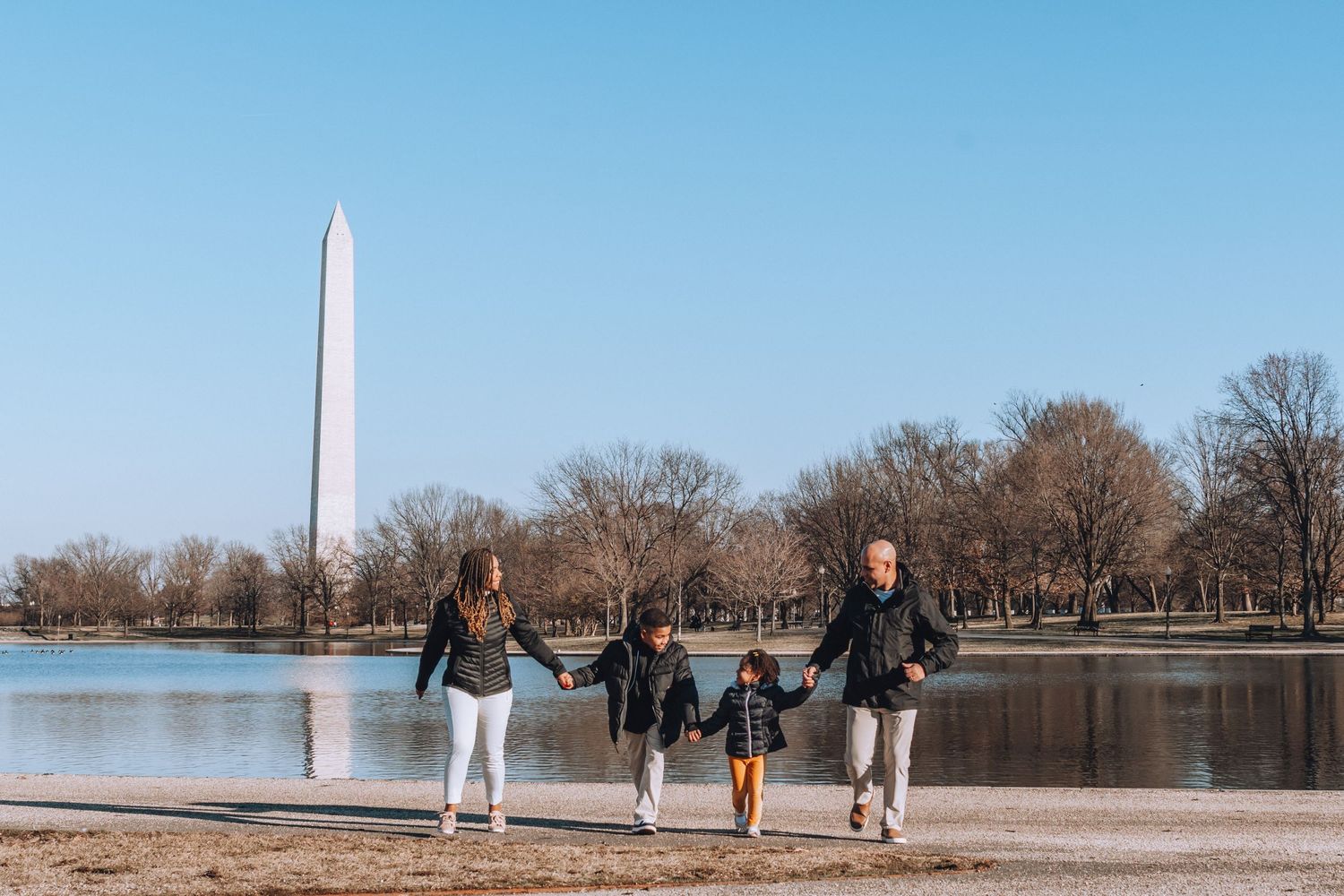 Family walking along waterfront path with Washington Monument visible across the reflecting pool.