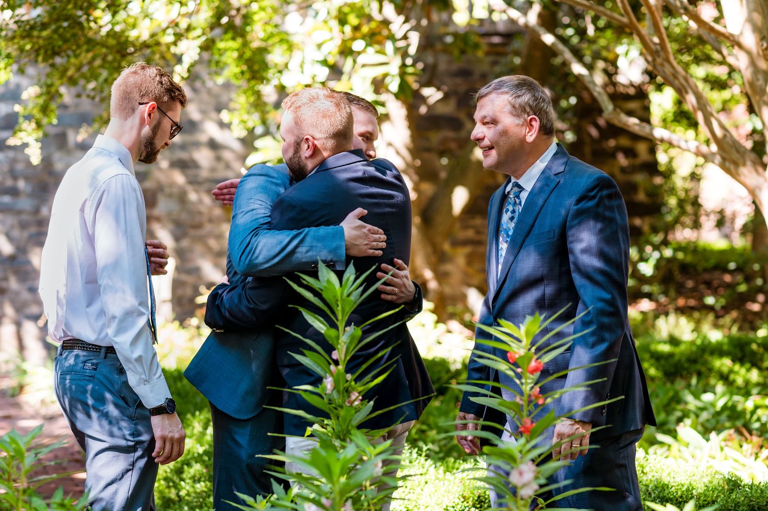 Emotional group hug during outdoor wedding celebration in garden setting.