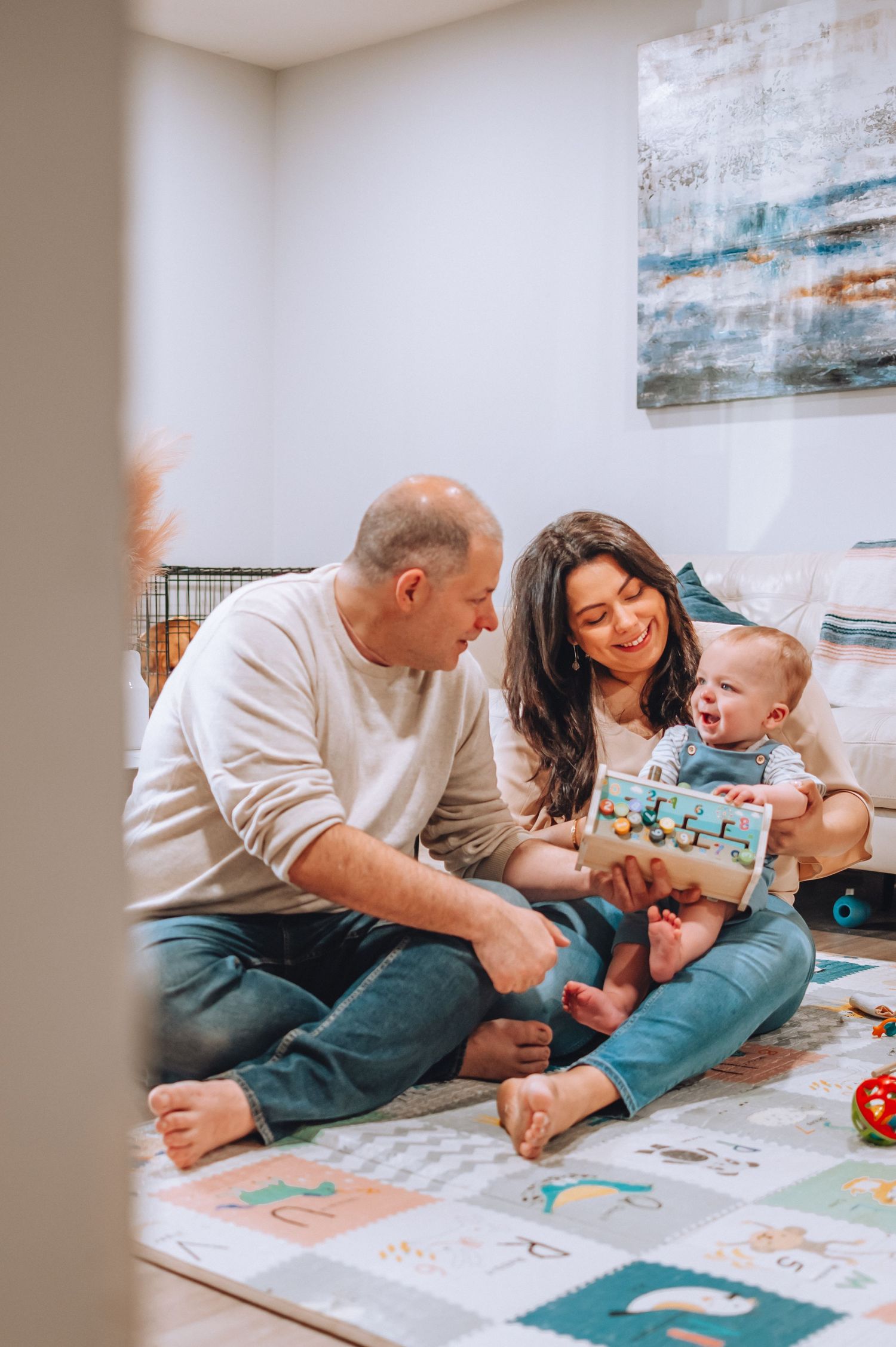Family sitting together on playmat with baby, enjoying indoor playtime.