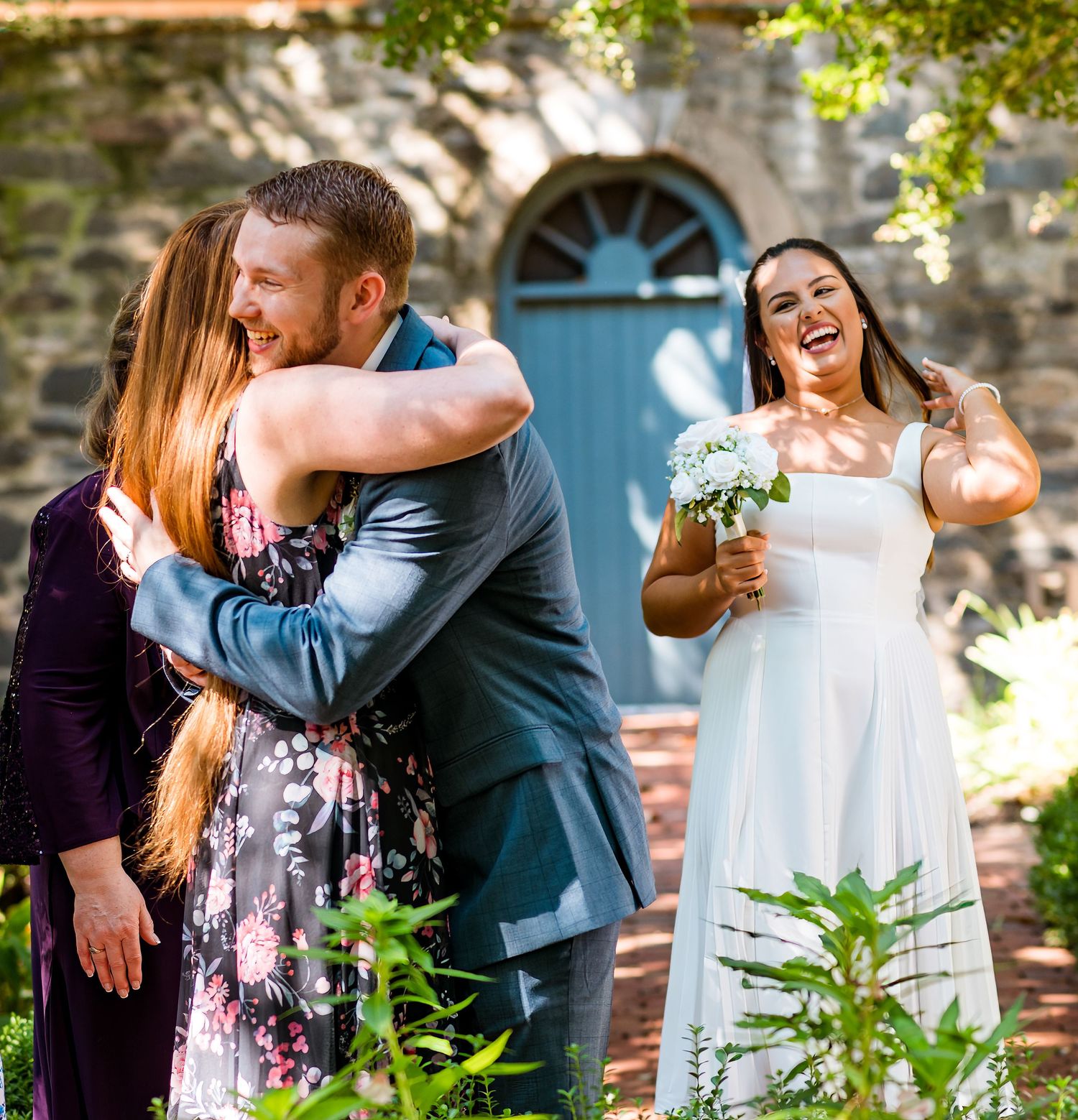 Wedding celebration with guests sharing hugs and laughter in garden setting.