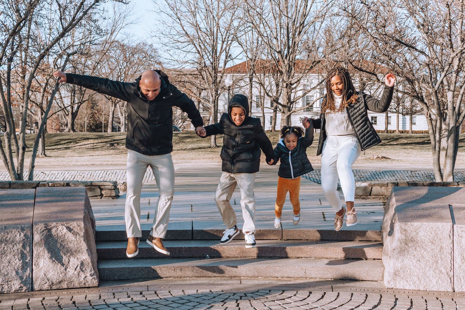 Family jumping together on stone steps in park during winter season.