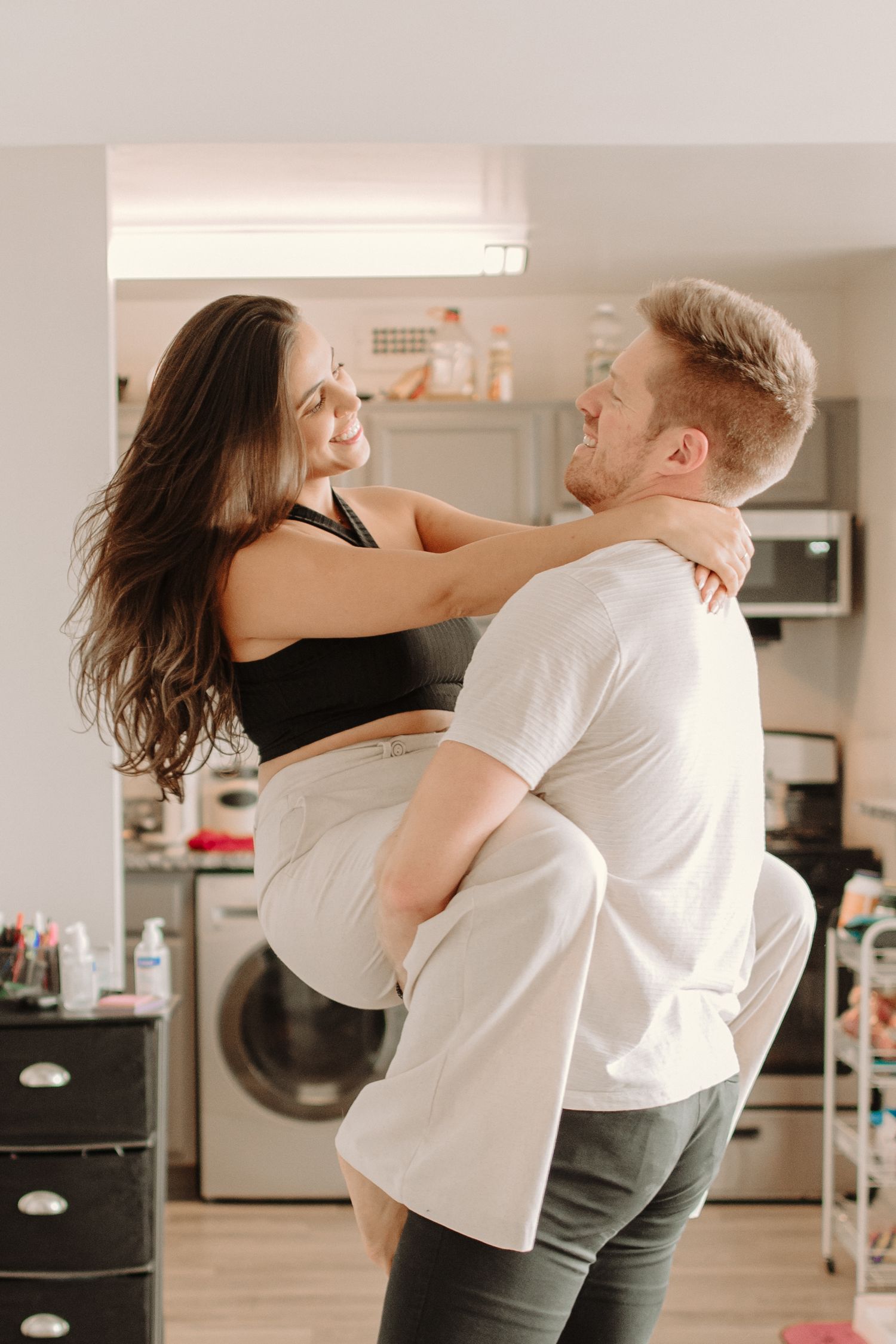 A couple dancing and embracing in a home setting with household appliances visible in the background.