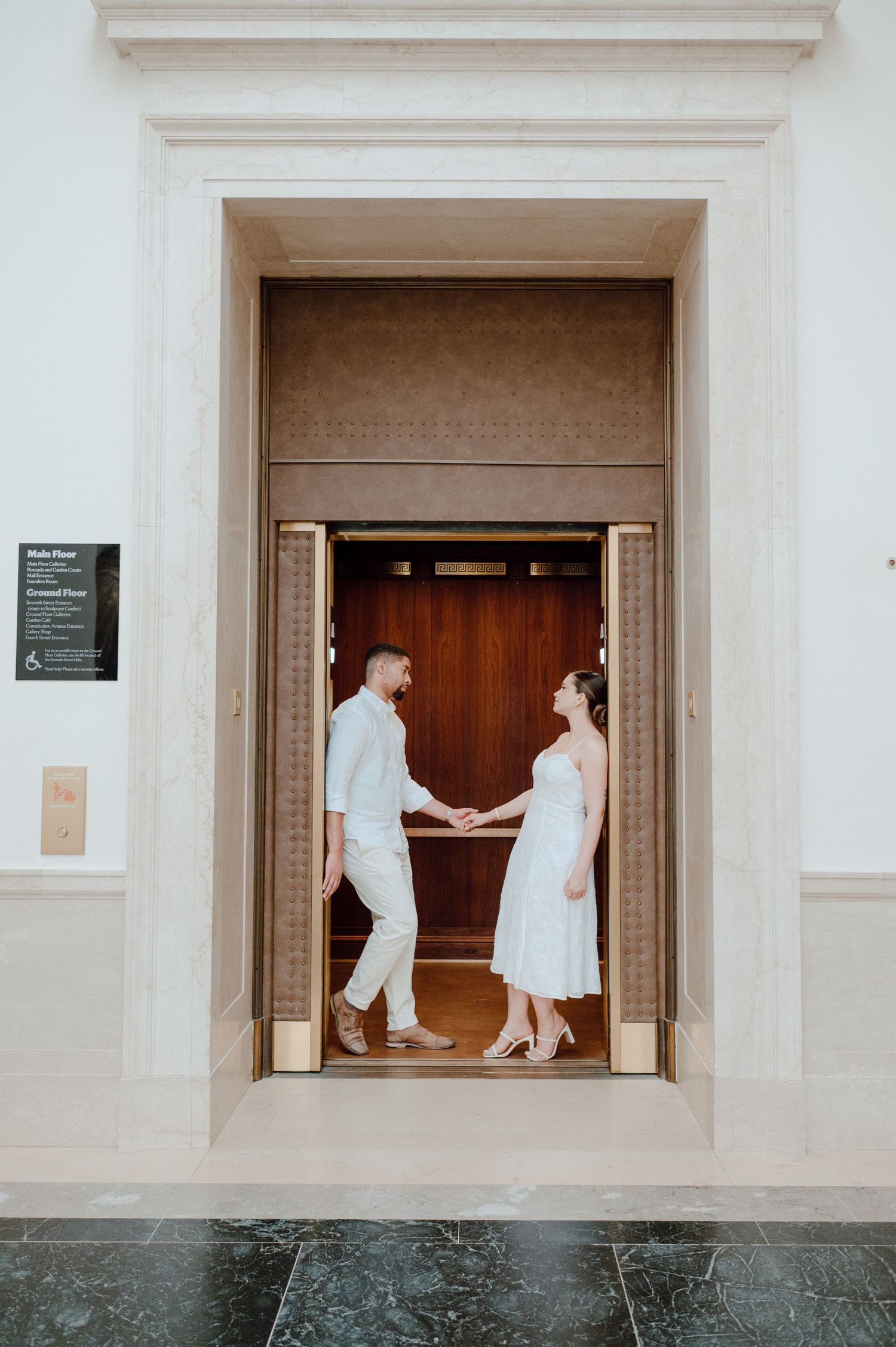 A couple holding hands while standing in an ornate doorway of a historic building.