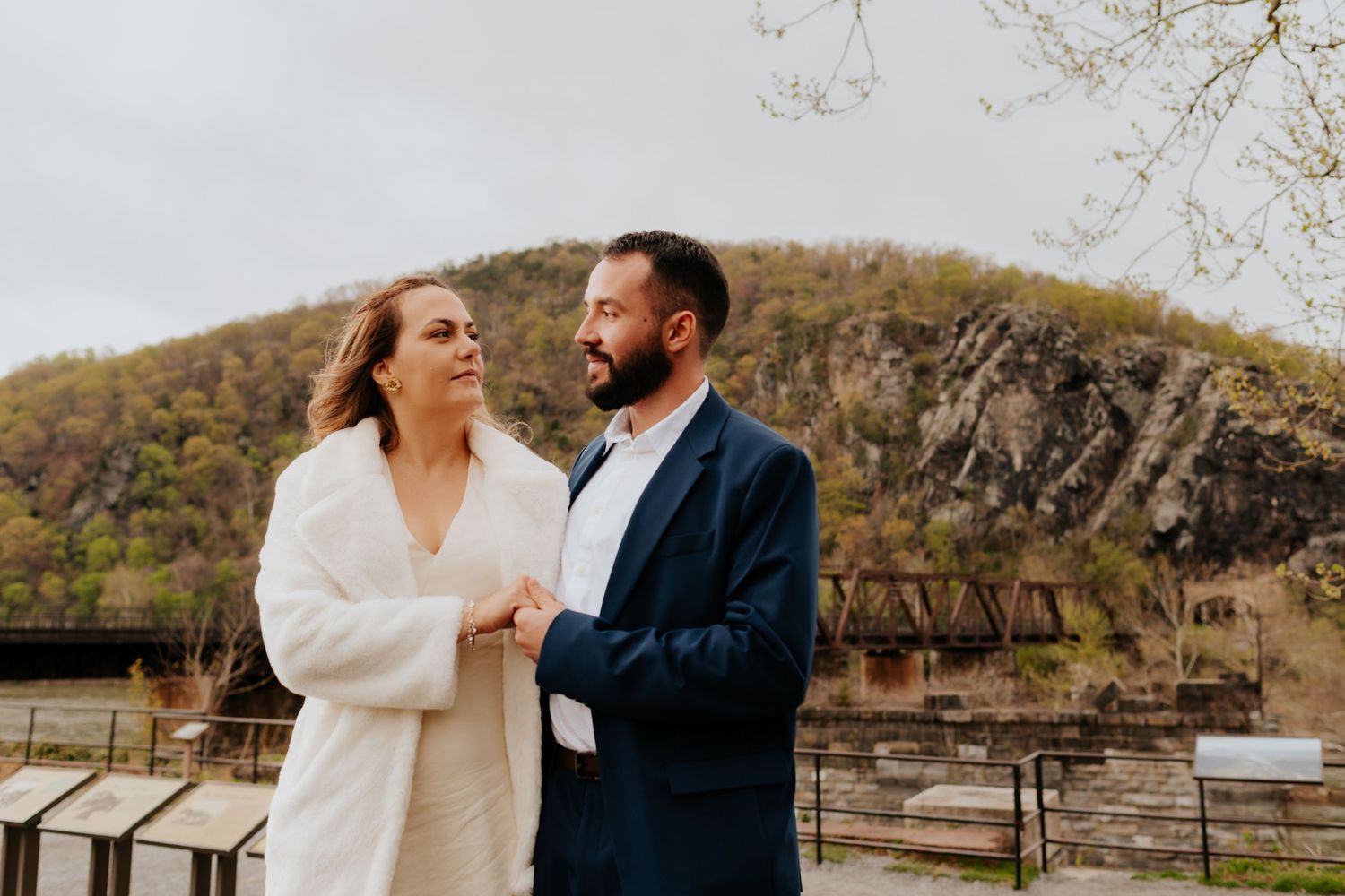 A couple shares a romantic moment by a rustic wooden fence on a hillside at sunset.