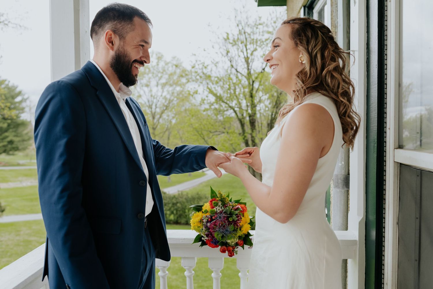 A shared first look wedding moment between a bride in white and groom in navy blue suit during an outdoor ceremony.