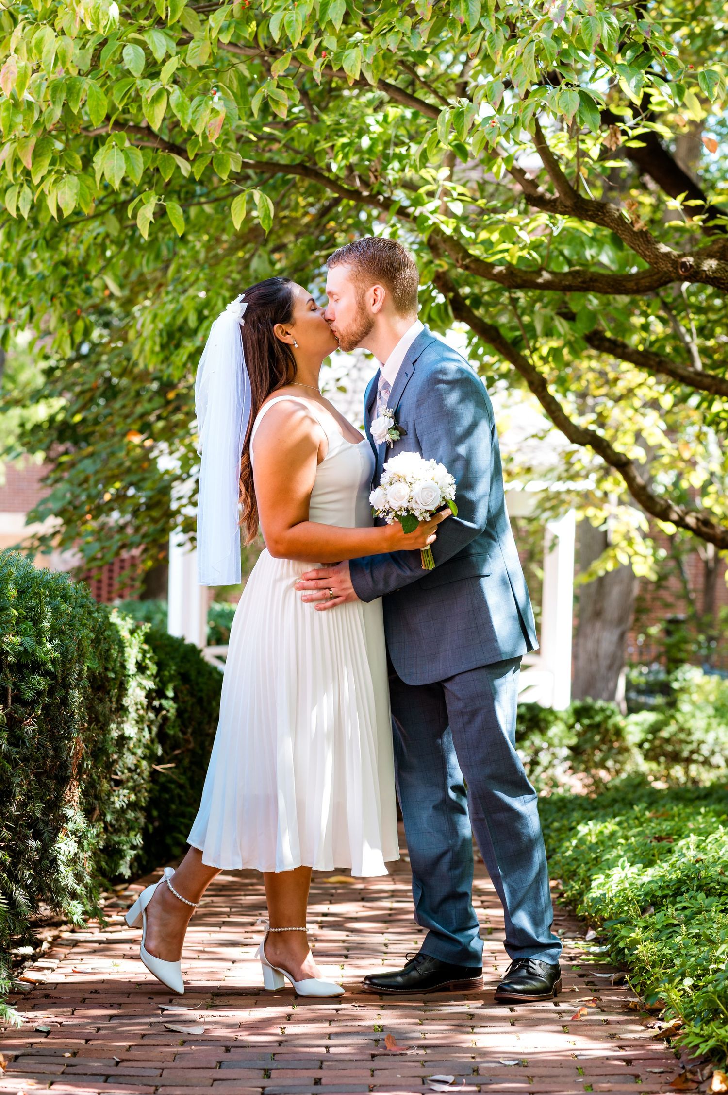 Romantic moment between newlyweds on a brick garden path surrounded by green foliage.