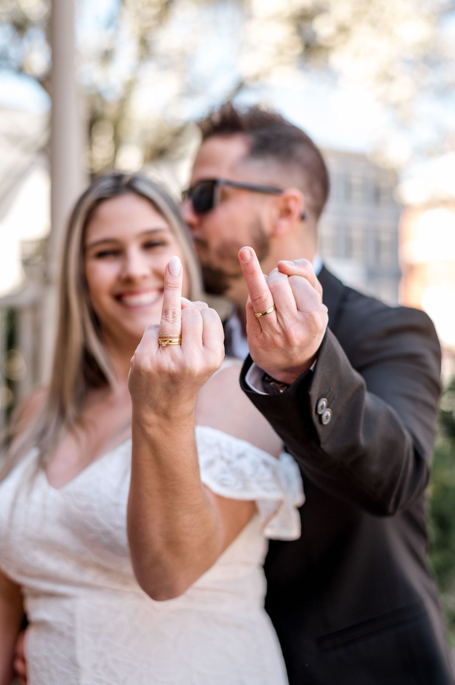 Newlywed couple showing off their wedding rings with joyful expressions outdoors.