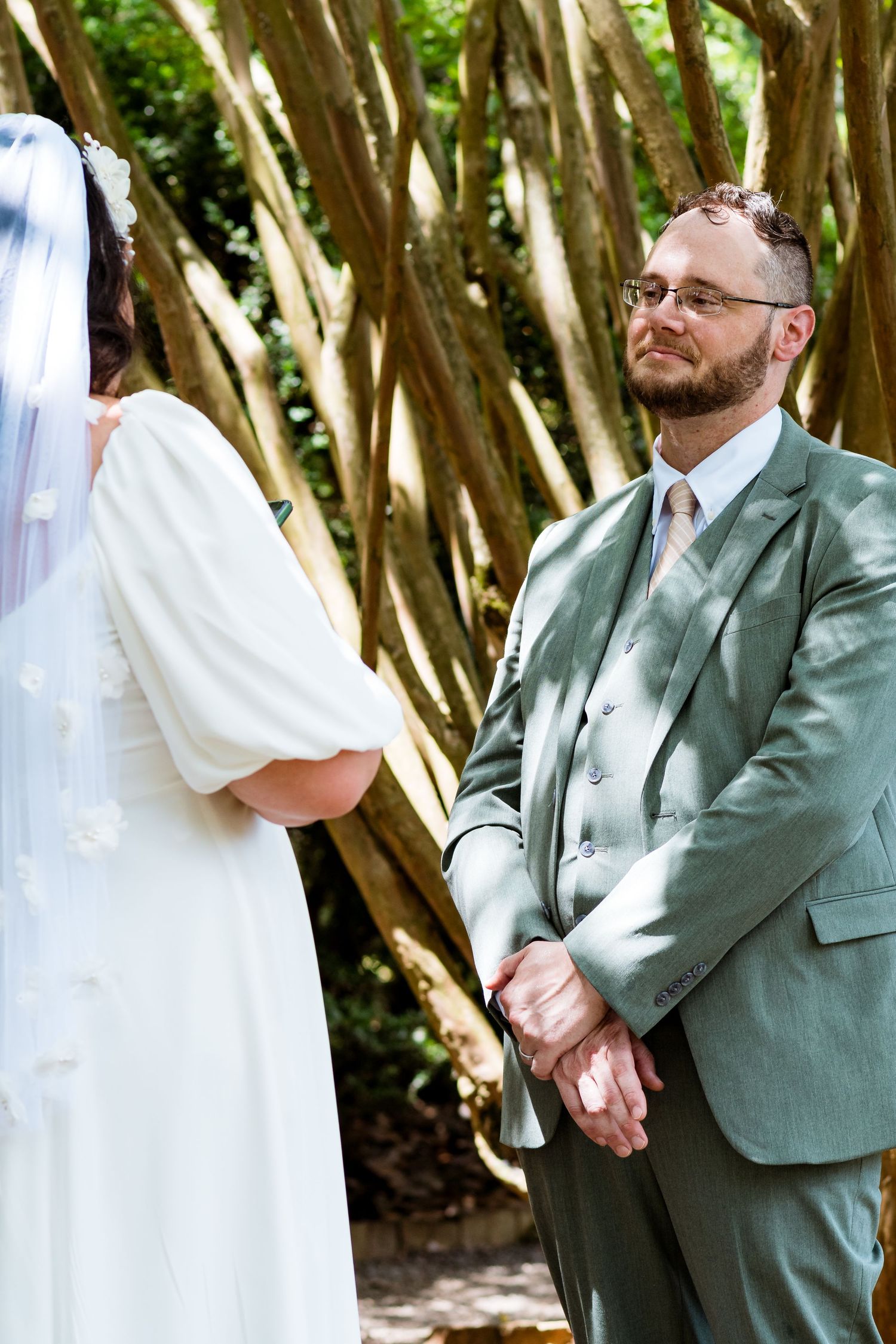 Couple sharing an intimate moment during their wedding ceremony under trees.