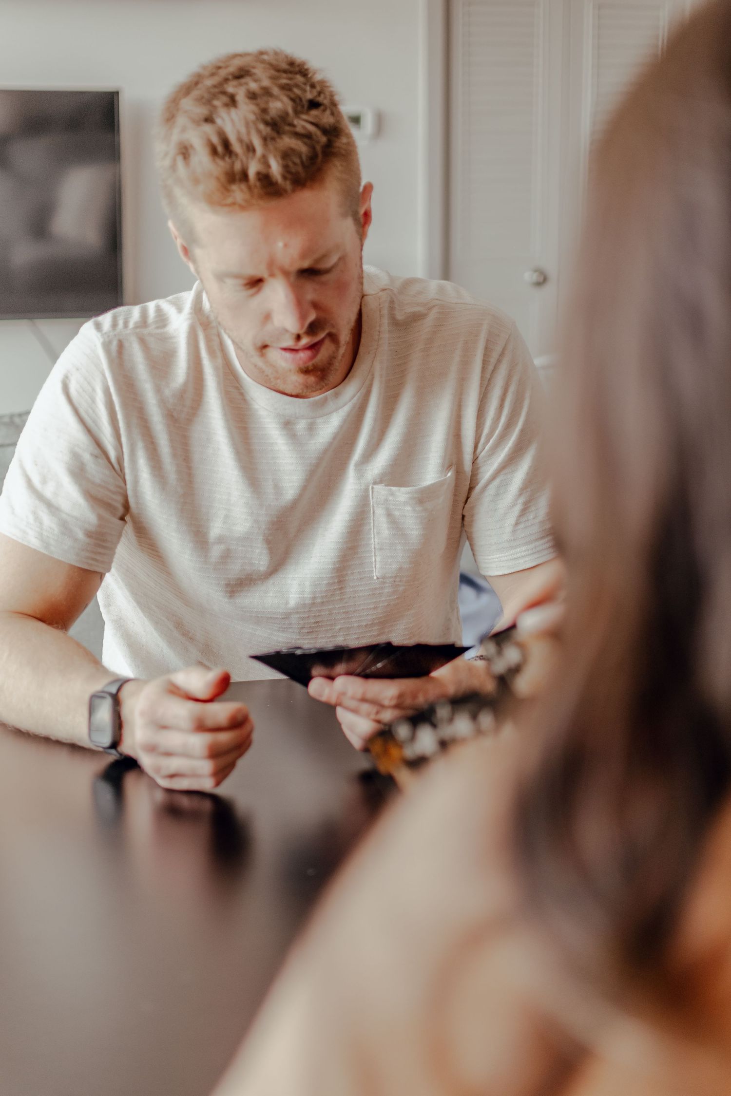 Person in white t-shirt looking down at something while seated indoors.