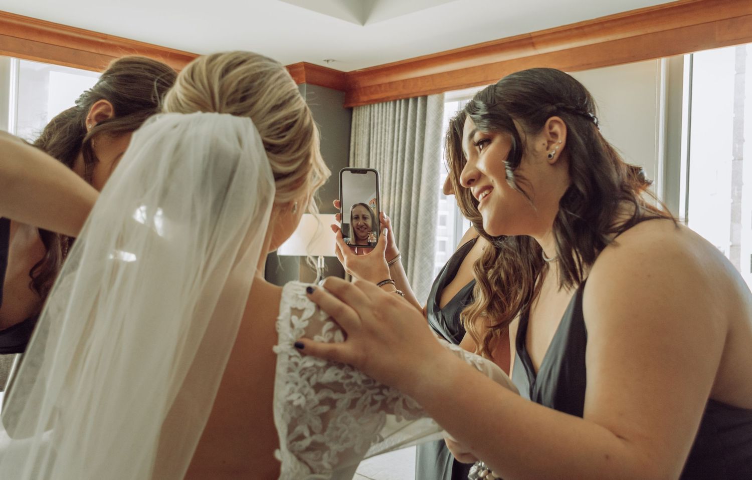 Bridesmaids in dark dresses gather around to look at phone during wedding preparations.