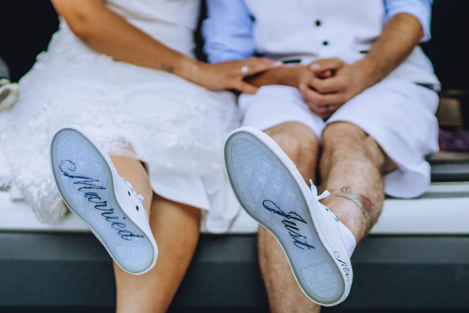 Close up of two pairs of feet wearing 'Just Married' inscribed sneakers while sitting on white fabric.