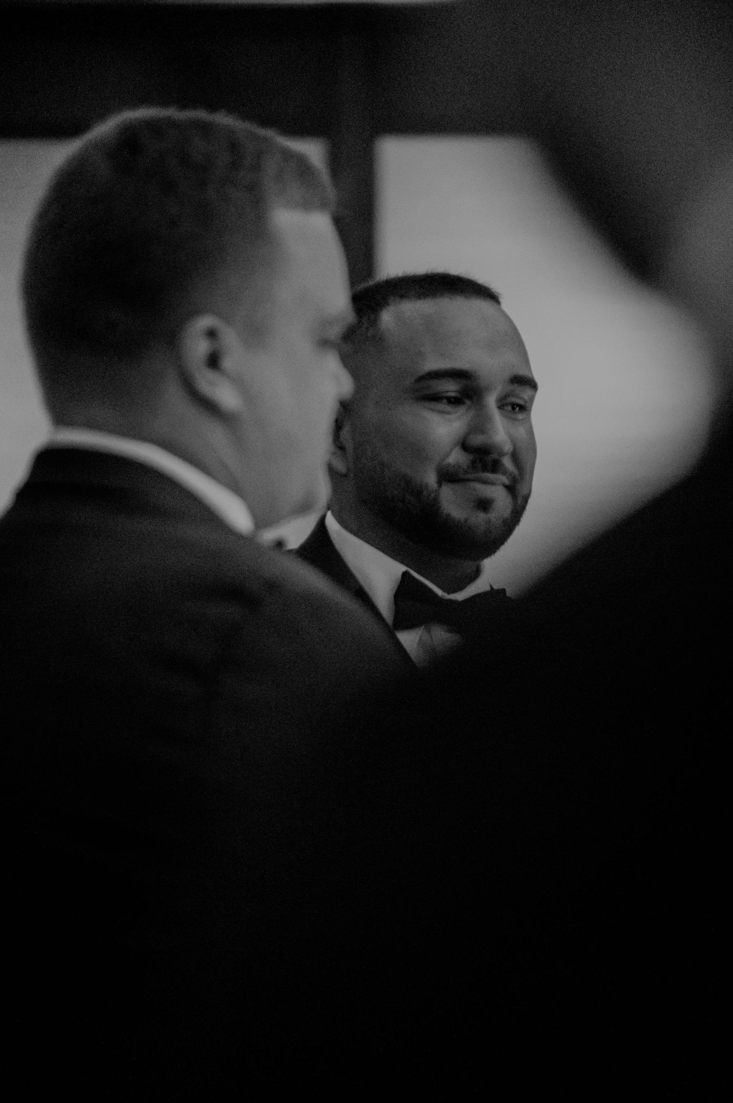 A black and white candid portrait of two men in formal attire engaged in conversation at an event.