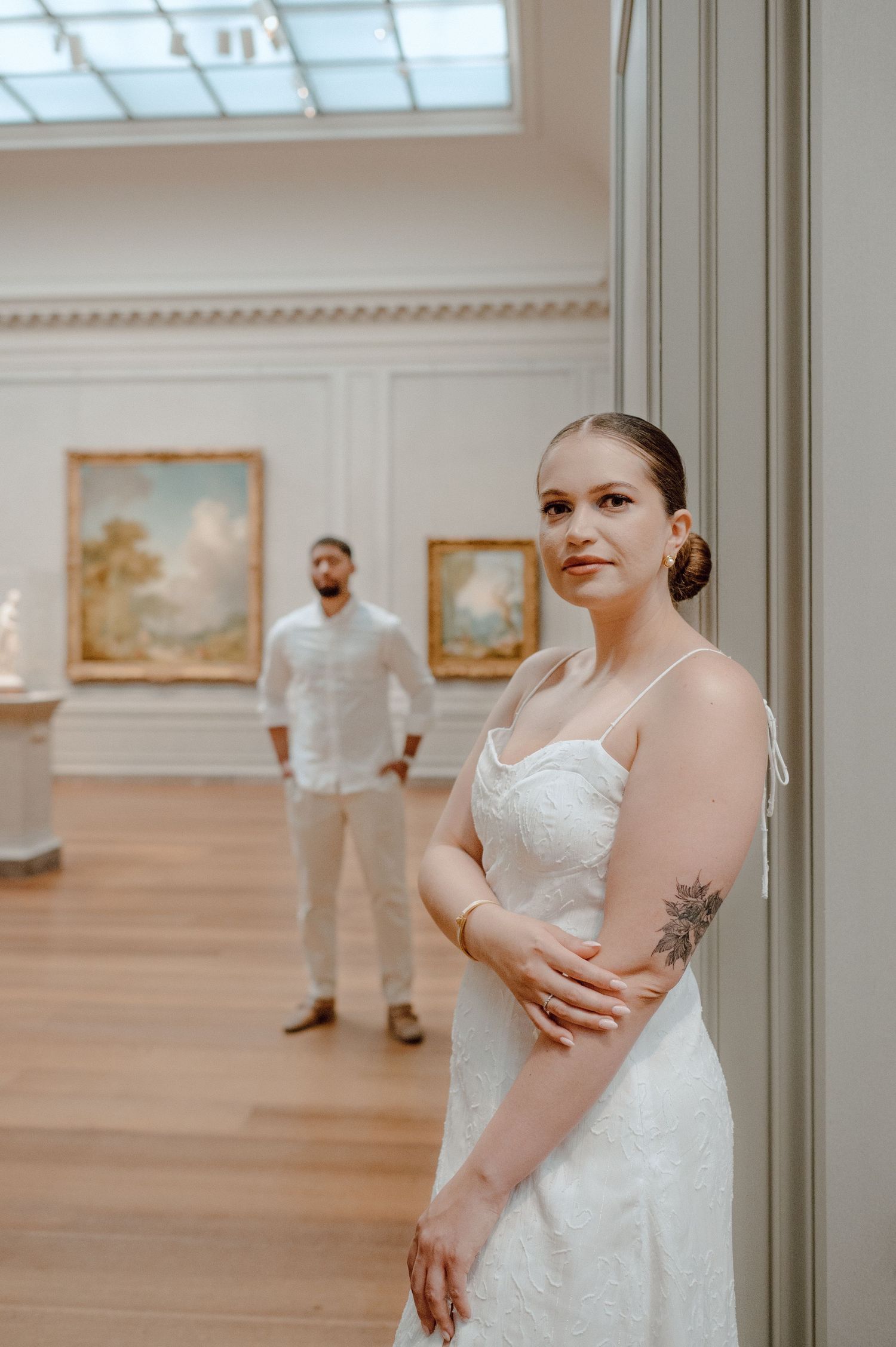 Intimate gallery portrait featuring a couple in matching white outfits surrounded by classical paintings.