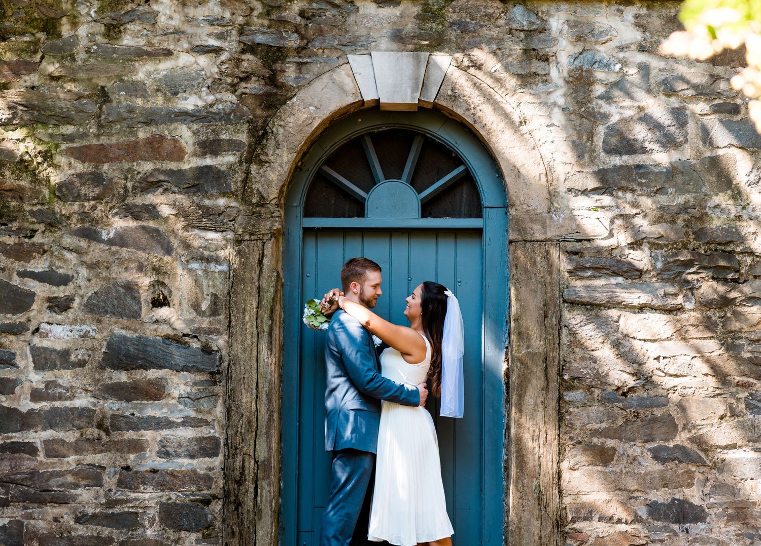 Couple sharing intimate moment in front of blue arched doorway.