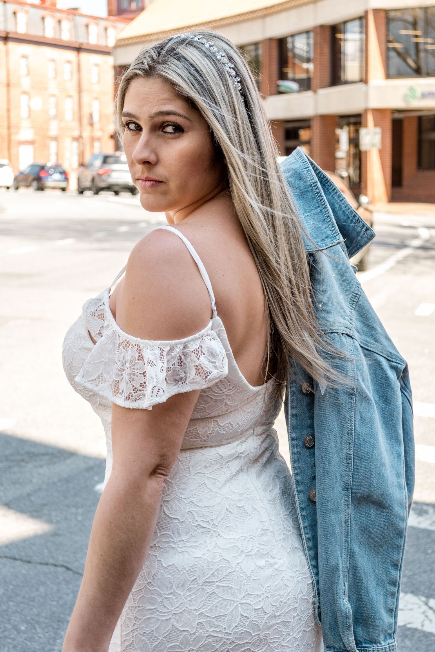 Bride wearing white lace dress with denim jacket in urban setting.