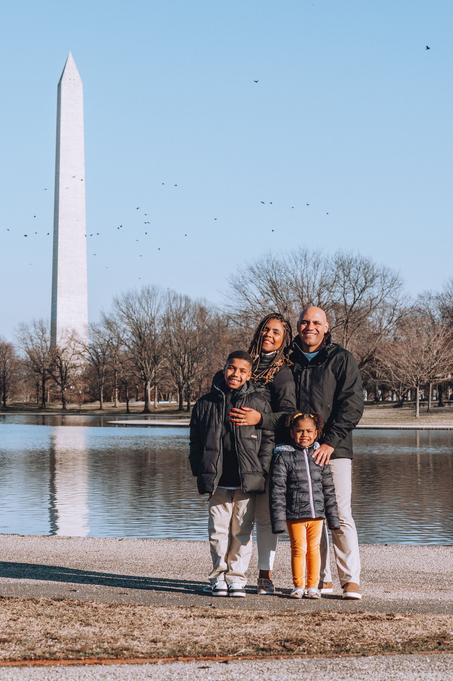 Family poses together by the reflecting pool with Washington Monument in background at National Mall.