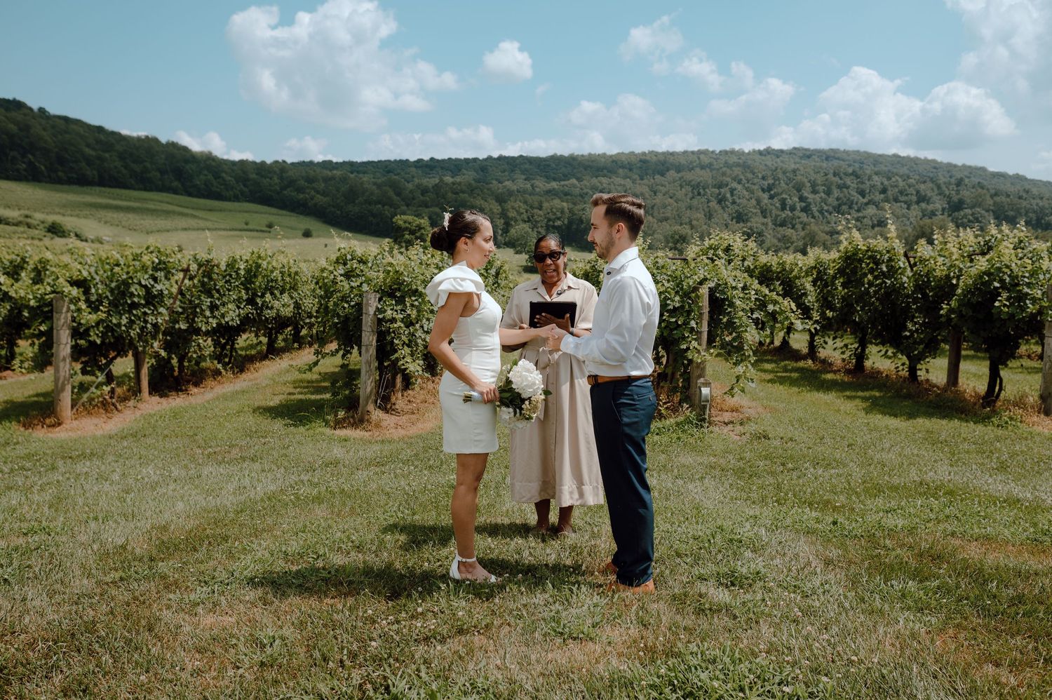 A couple shares a romantic moment among rows of grapevines at a scenic vineyard on a beautiful sunny day.