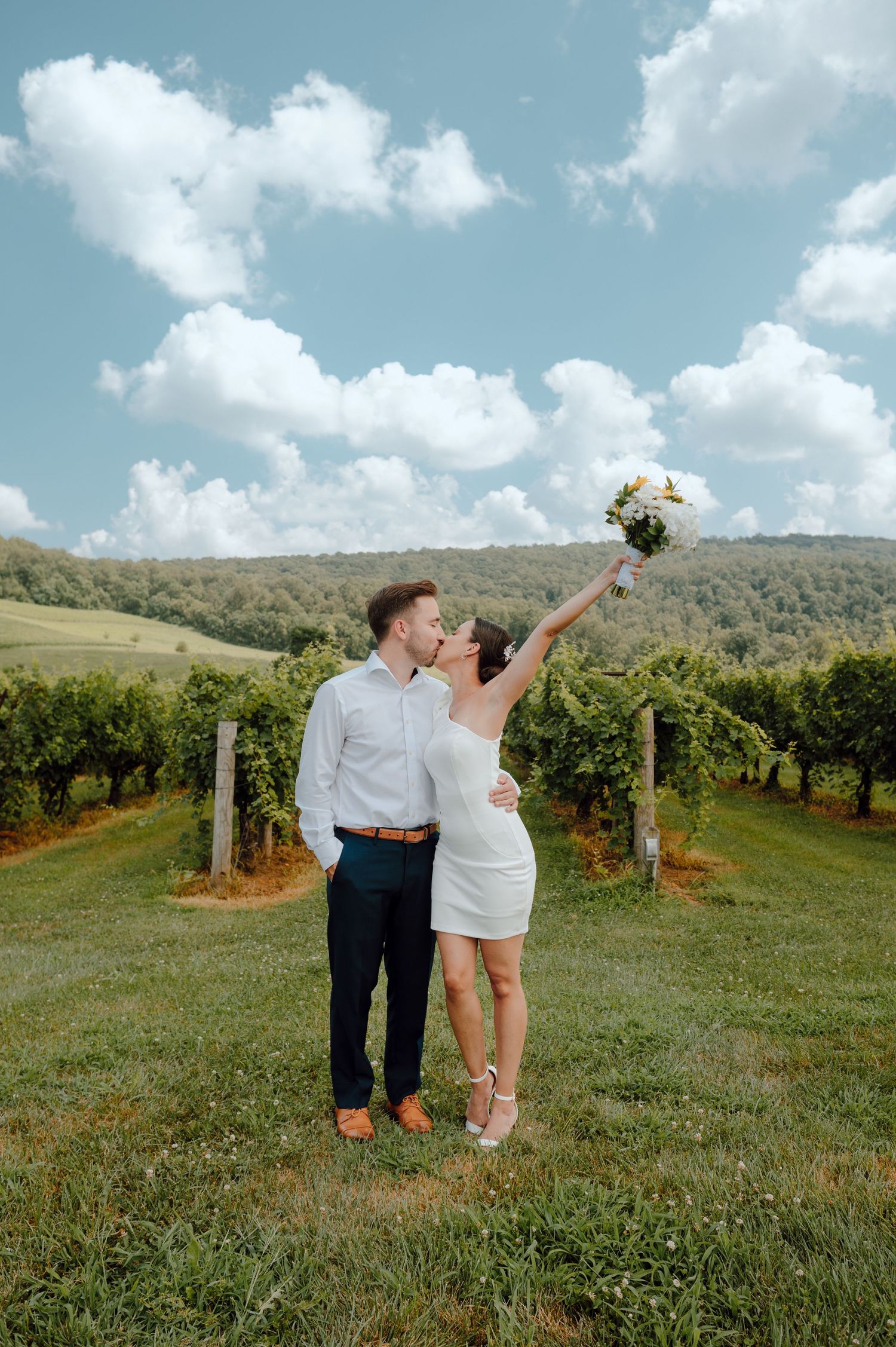A couple celebrates their wedding day at a scenic vineyard on a beautiful cloudy afternoon.