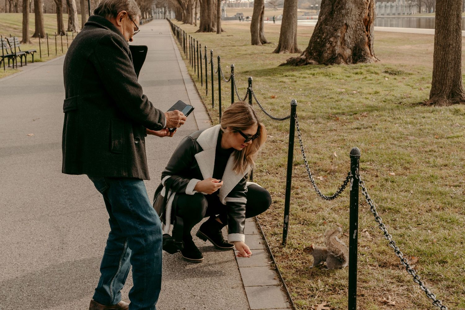 Two people taking photos of something on a park path surrounded by trees.