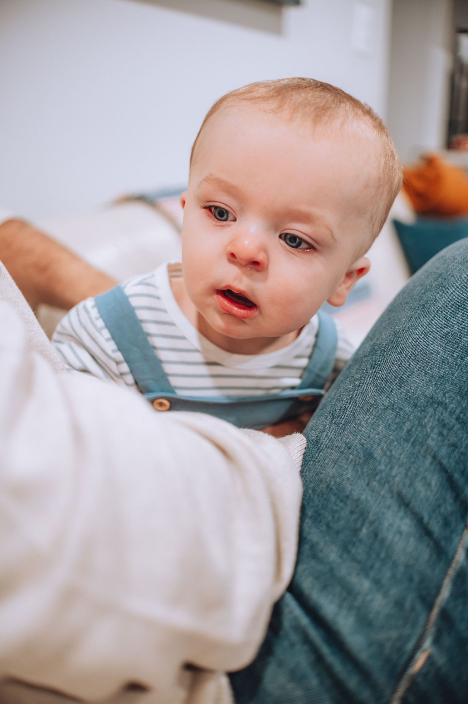 Baby wearing blue and white striped overalls lying on couch cushions.
