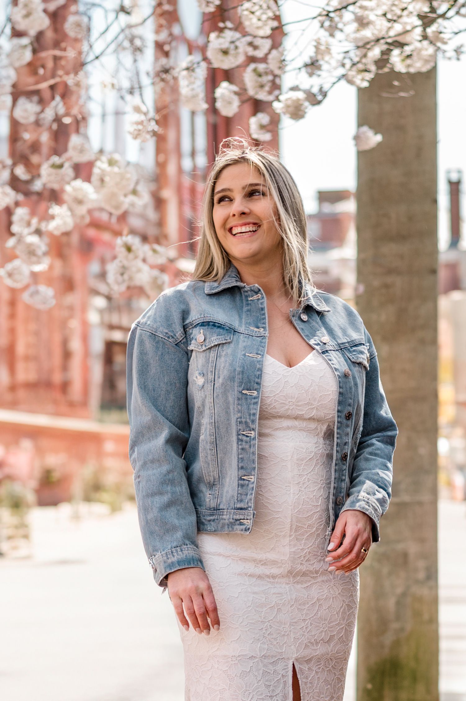 Spring wedding photo with cherry blossoms and bride wearing denim jacket over white dress.