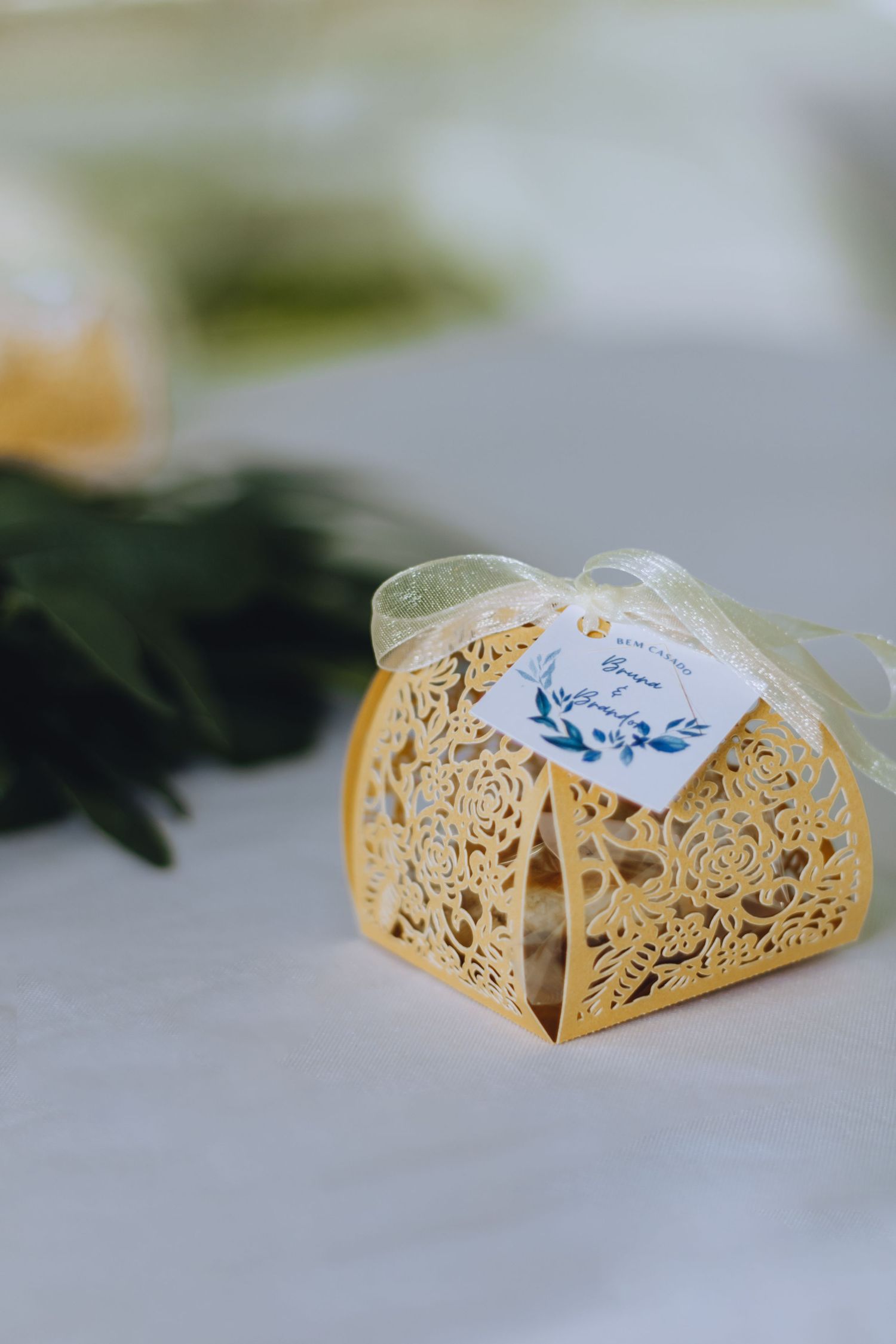Delicate golden laser-cut favor box with ornate floral design and small blue tag on white surface.