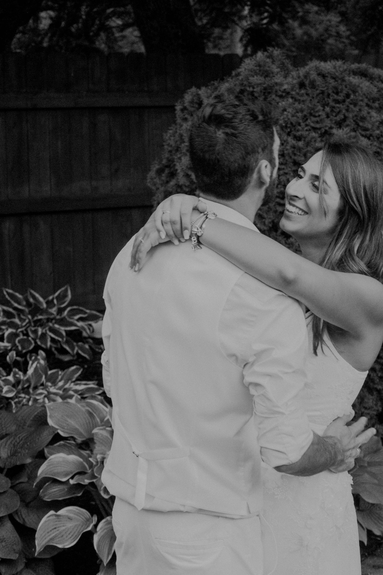 A tender black and white moment between a couple embracing outdoors in a garden setting.