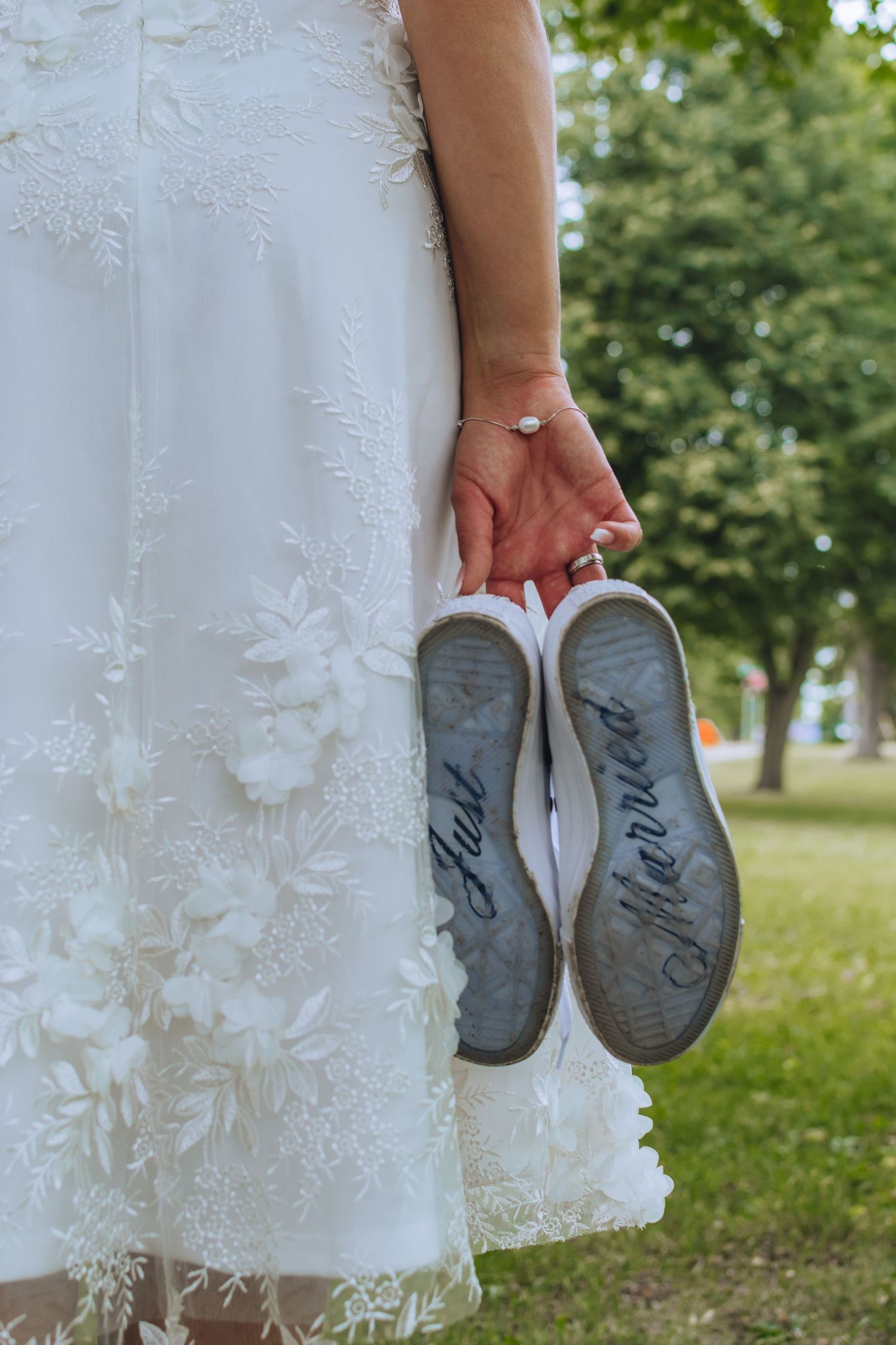 A bride in a white lace dress holds her wedding shoes showing 