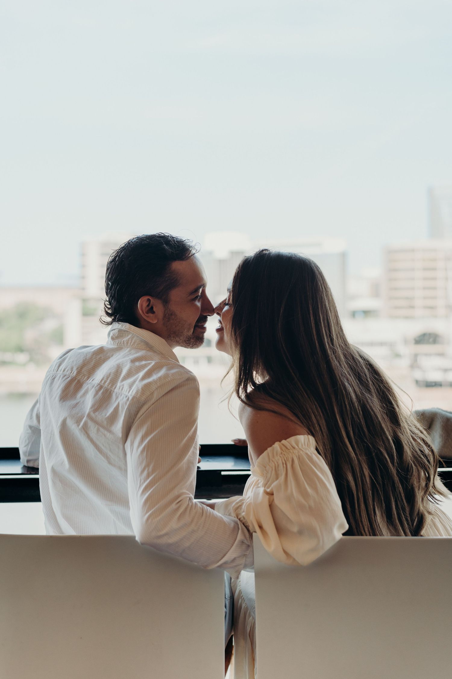 A romantic couple shares an intimate moment on a balcony overlooking a cityscape.