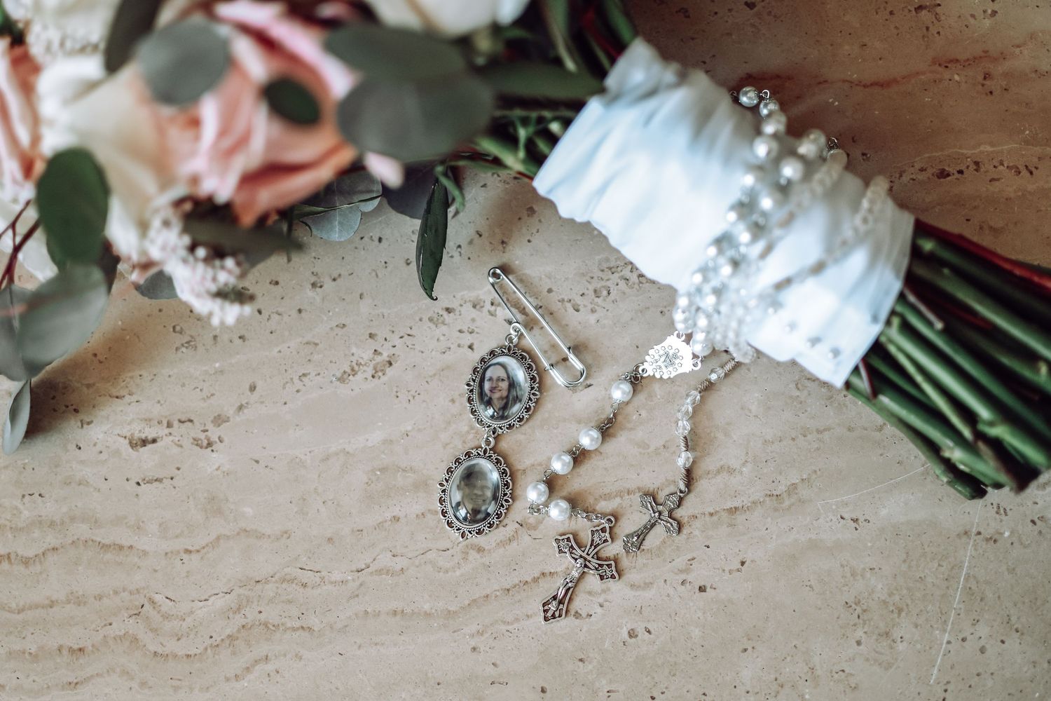 A sparkly wedding ring sits on a wooden surface next to pink and white flowers and scattered jewels.
